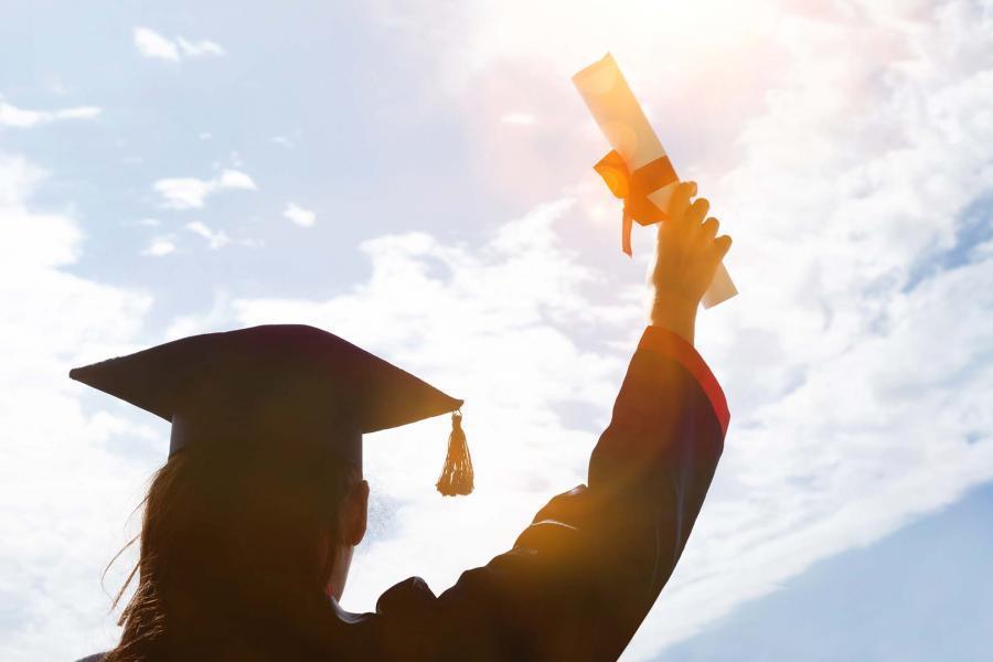 girl in cap and gown holding rolled diploma in the air